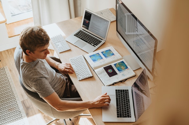 man working at desk with two laptops plus one monitor