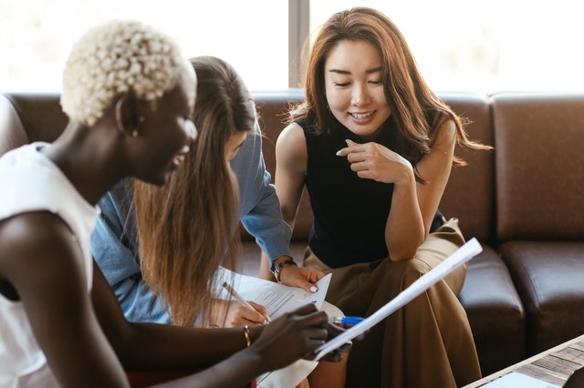 three people sitting on leather couch looking over paperwork 